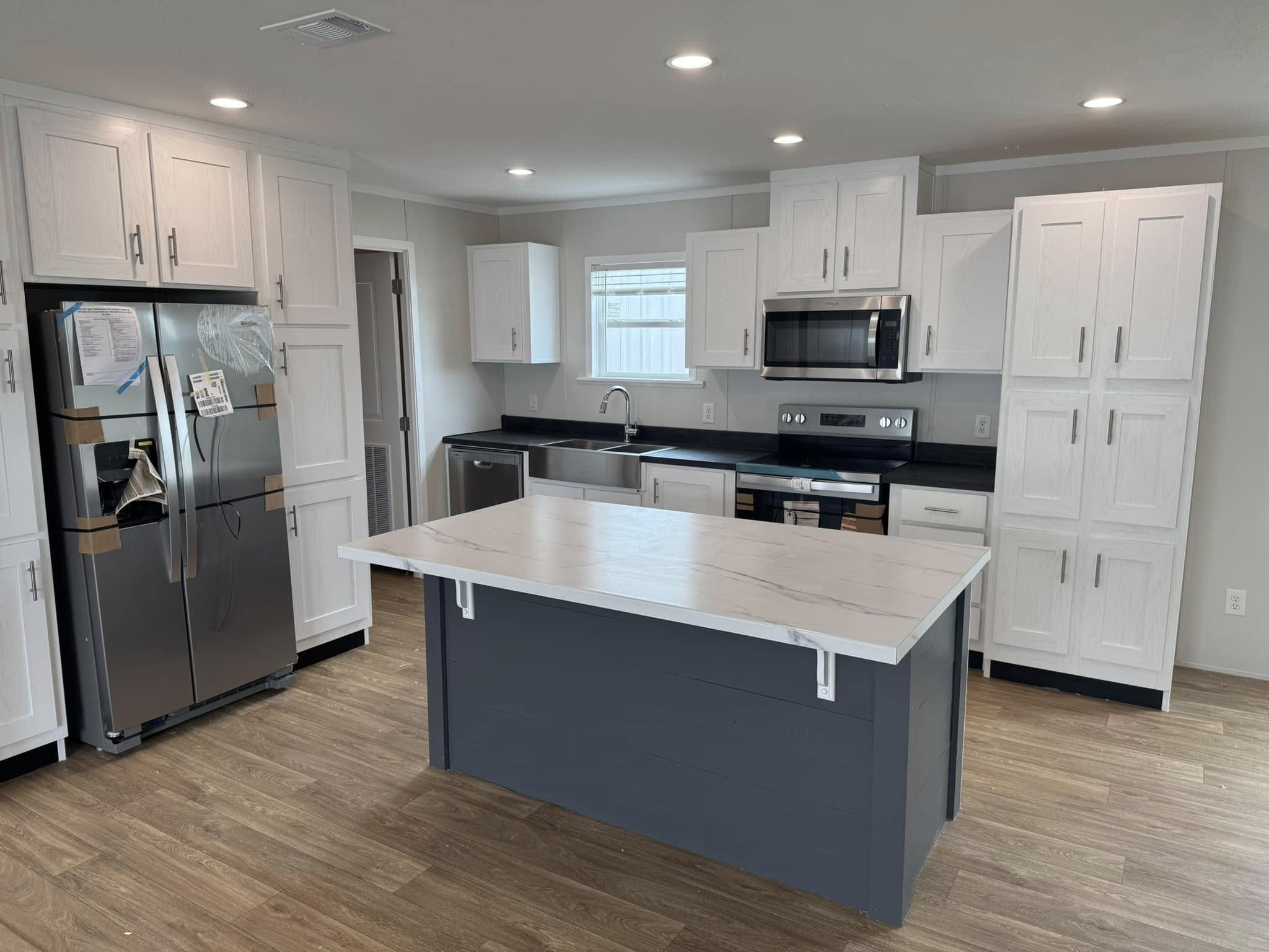 Modern kitchen with a sleek gray island, stainless steel appliances, white cabinetry, and wood flooring. Bright and inviting ambiance.