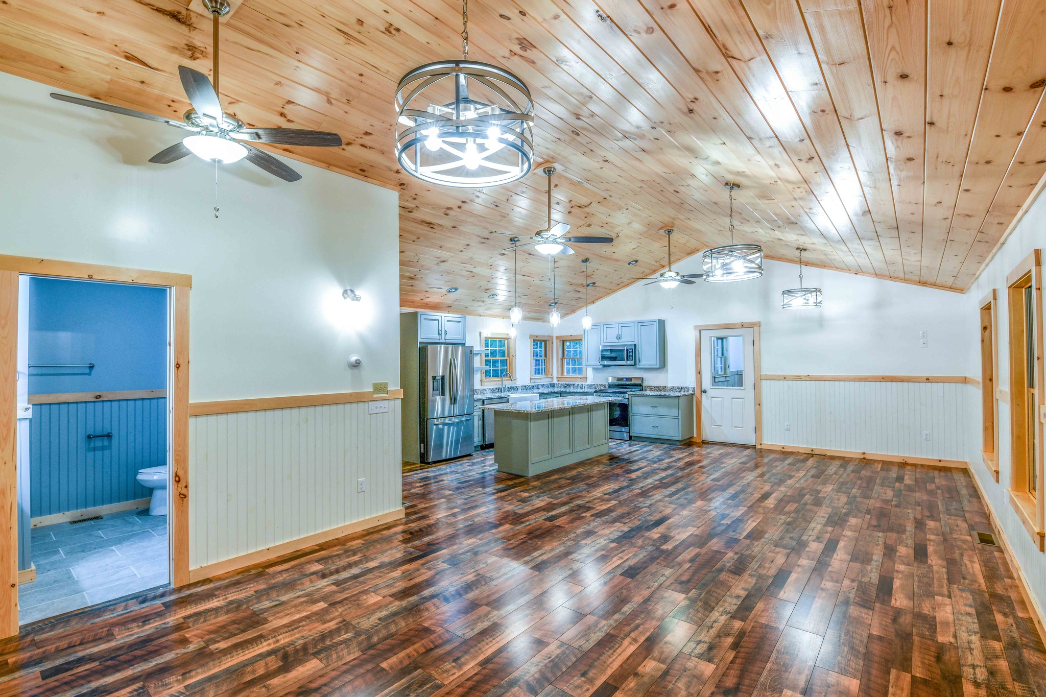 Spacious open-concept kitchen and dining area with wooden floors and ceiling, modern stainless steel appliances, ceiling fans, and pendant lights. Cozy and inviting.