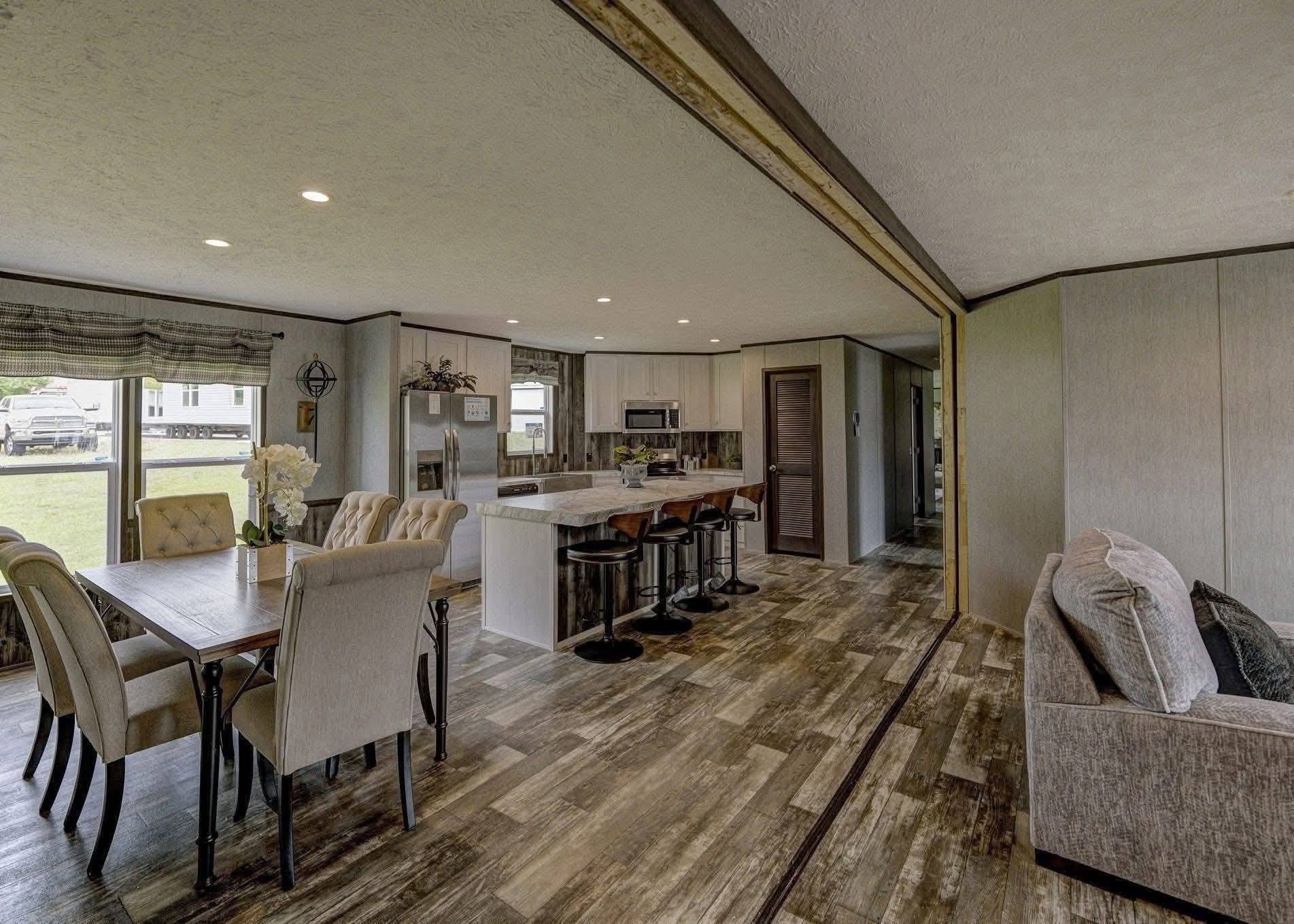 Spacious open-plan kitchen and dining area with rustic flooring. A wooden dining table with beige chairs is beside the kitchen island with bar stools. Cozy and inviting.