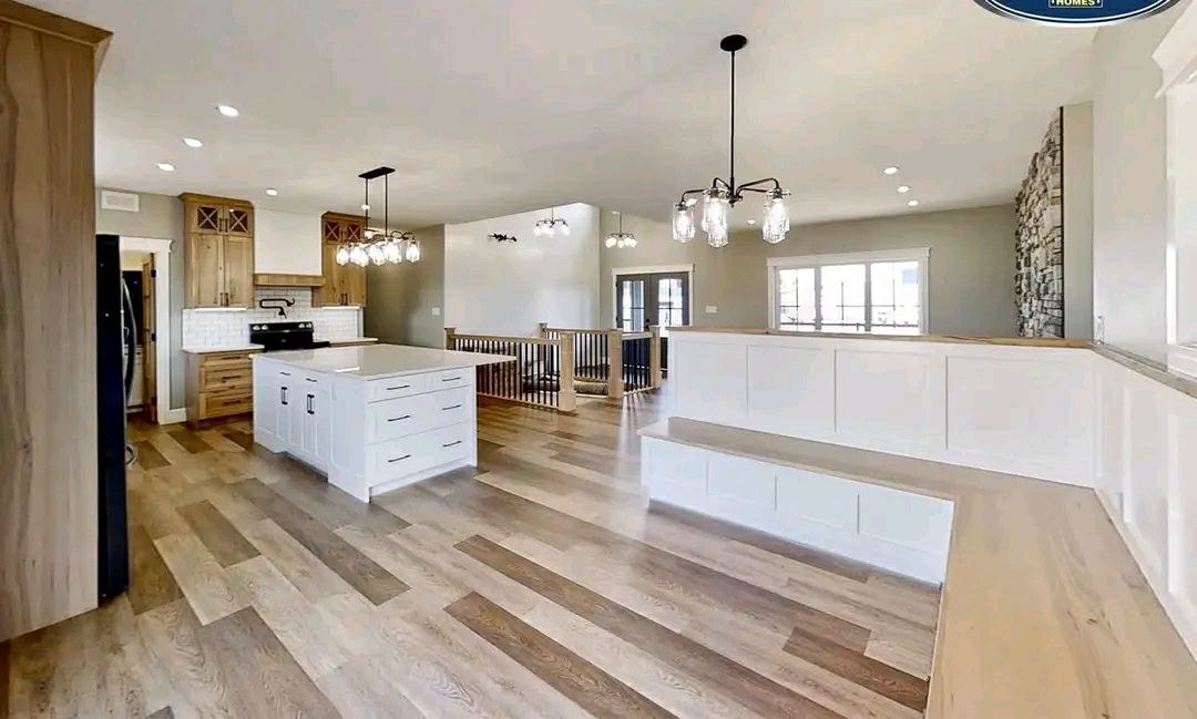 Spacious modern kitchen with light wood flooring, white island, and wooden cabinets. Pendant lights hang above, creating a bright, open atmosphere.