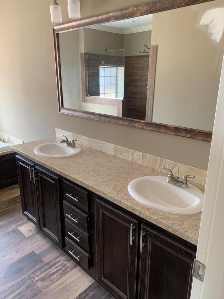 Modern bathroom with dual sinks on a tan granite countertop, dark wood cabinets, and a large wall mirror. Neutral tones and a clean, elegant look.