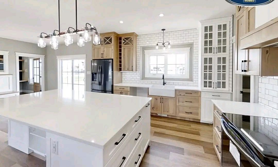 Spacious modern kitchen featuring a large white island, hanging lights, wooden cabinets, black fridge, farmhouse sink, and white subway tiles.