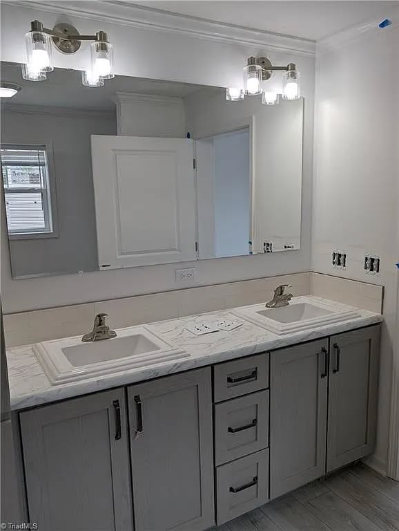 Modern bathroom with a dual sink vanity, marble countertop, and brushed metal faucets. A large mirror is above, flanked by sleek light fixtures, creating a clean and bright ambiance.