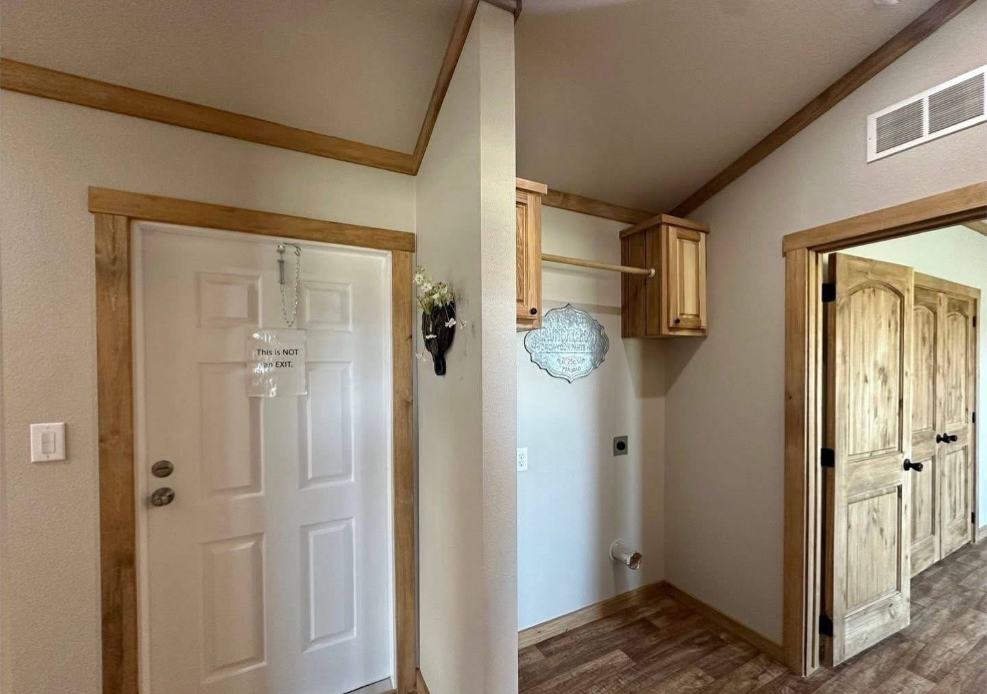 A small hallway features a white door with a sign saying "This is not an exit," light wood trim, an open closet with wooden cabinets, and decorative accents.