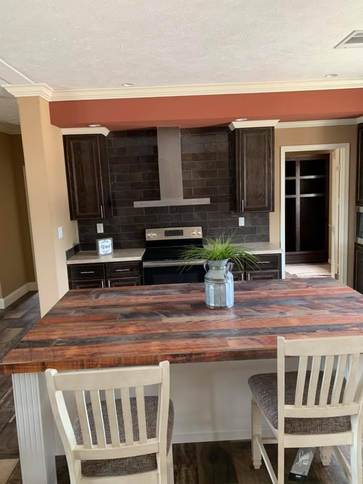 Modern kitchen with dark cabinets, black backsplash, and stainless steel appliances. A wooden island with two chairs and a small plant in a vase.