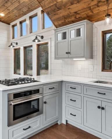 Chic kitchen with gray cabinets, white countertop, built-in oven, and stove. Large windows and wood ceiling create a warm, rustic ambiance.
