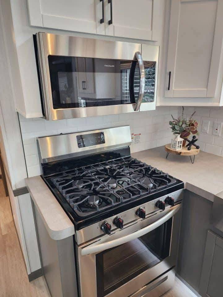 Modern kitchen with a stainless steel stove and overhead microwave. White cabinets and a decorative plant on the counter convey a clean, contemporary feel.