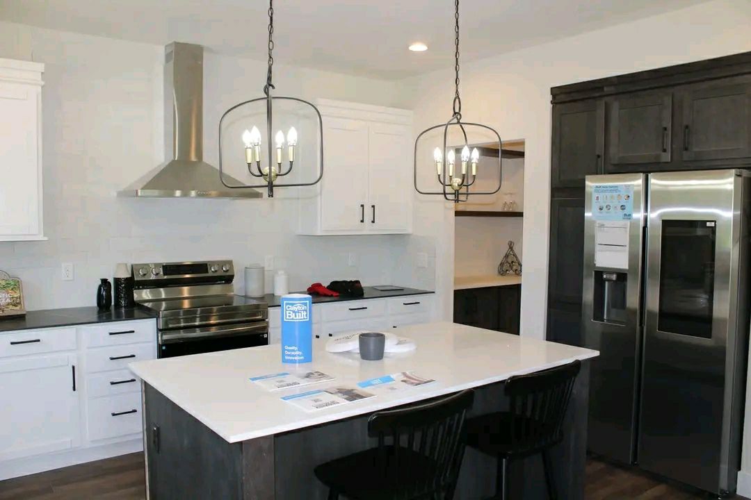 Modern kitchen with white cabinets, stainless steel appliances, and a large island. Two pendant lights hang above. Bright and organized atmosphere.