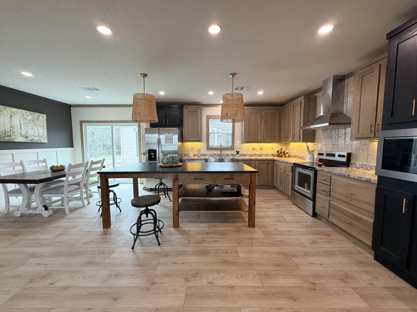 Spacious modern kitchen with light wood floors, island with barstools, sleek appliances, and dining area. Warm lighting and neutral tones convey coziness.