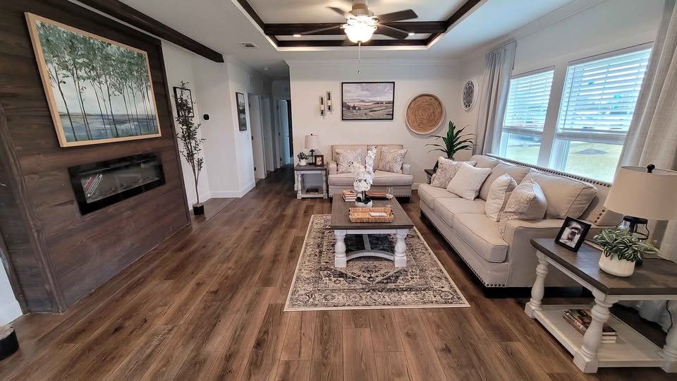 Cozy living room with wooden floors and contemporary decor. Features two beige sofas, a rug, a framed wall painting, and large windows with blinds.