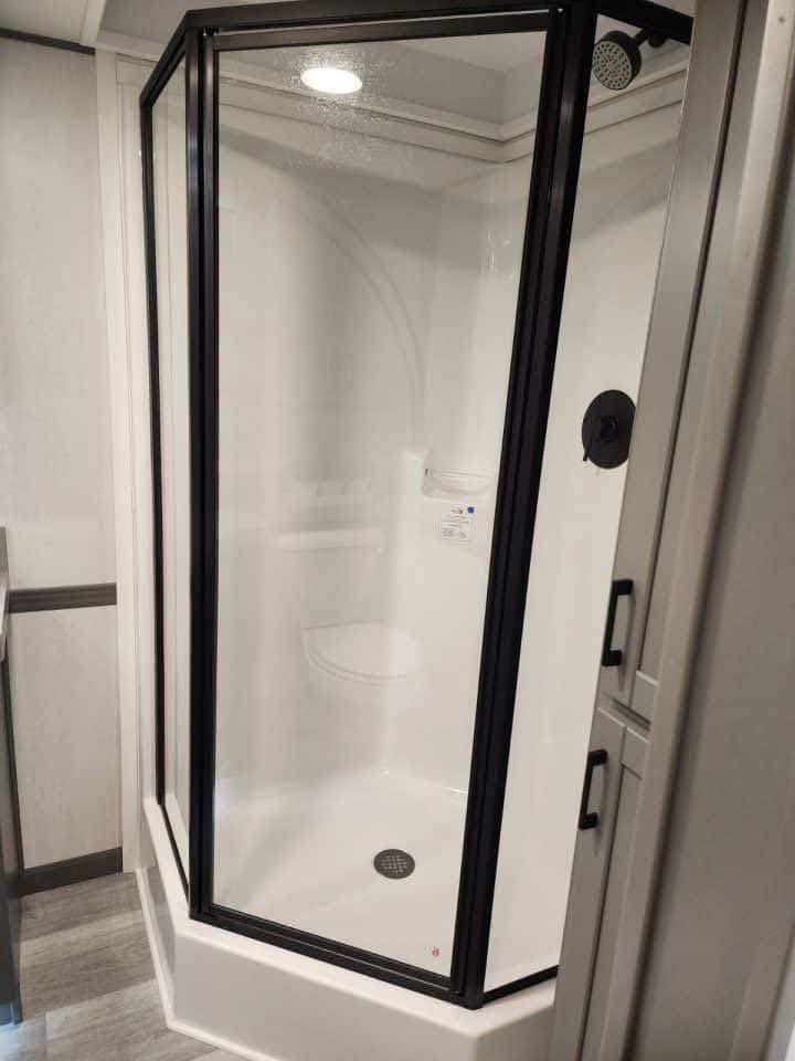 A compact, modern shower with clear glass panels and black frames in a bright bathroom. The floor and walls are light gray, conveying a clean, minimalist feel.