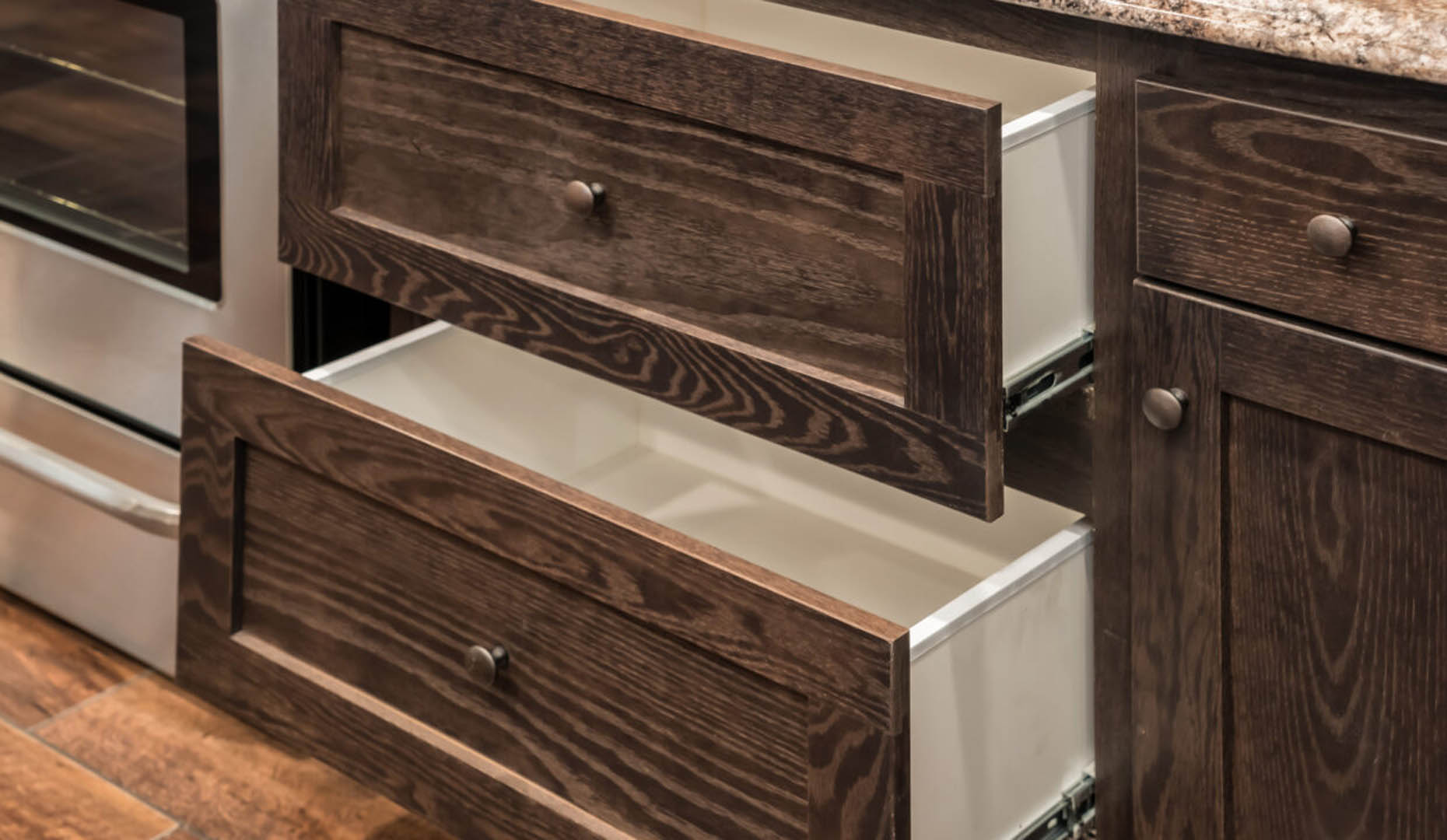 Open wooden kitchen drawers with visible grain texture, next to a stainless steel oven. The setting has a warm and rustic feel.