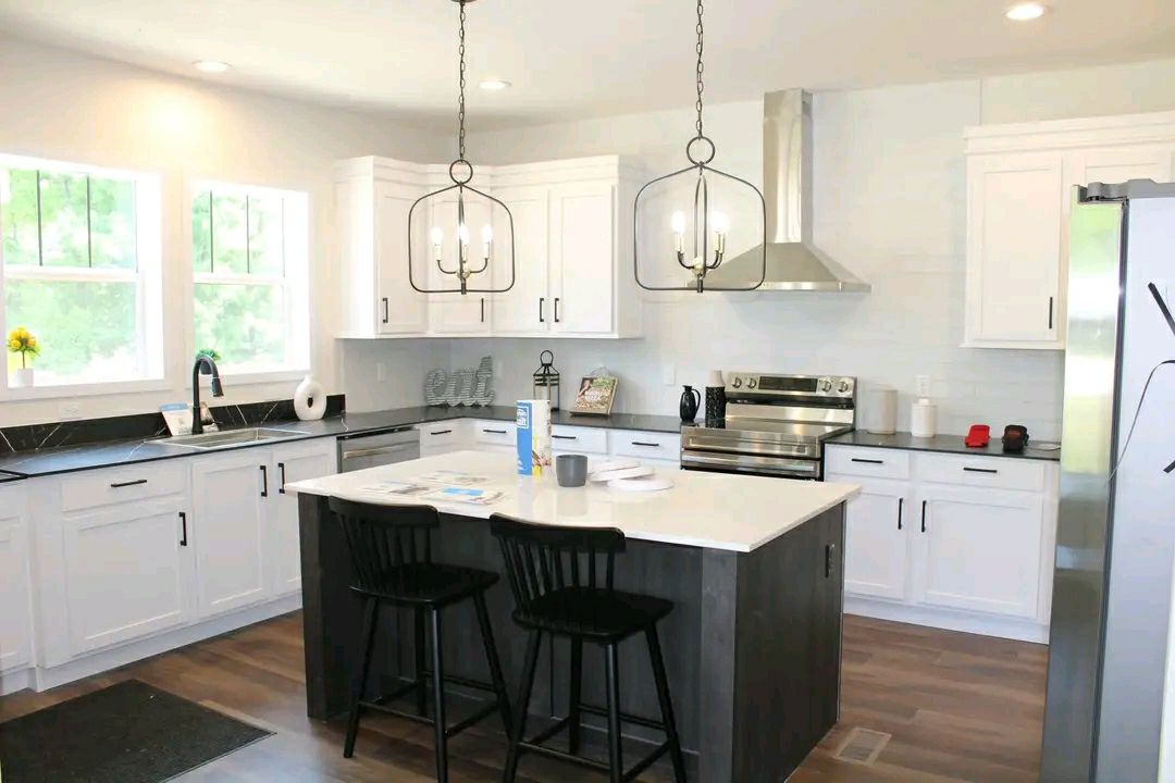 Modern kitchen with white cabinets, stainless steel appliances, and a central island with two black stools. Two pendant lights hang above the island, creating a bright, inviting atmosphere.