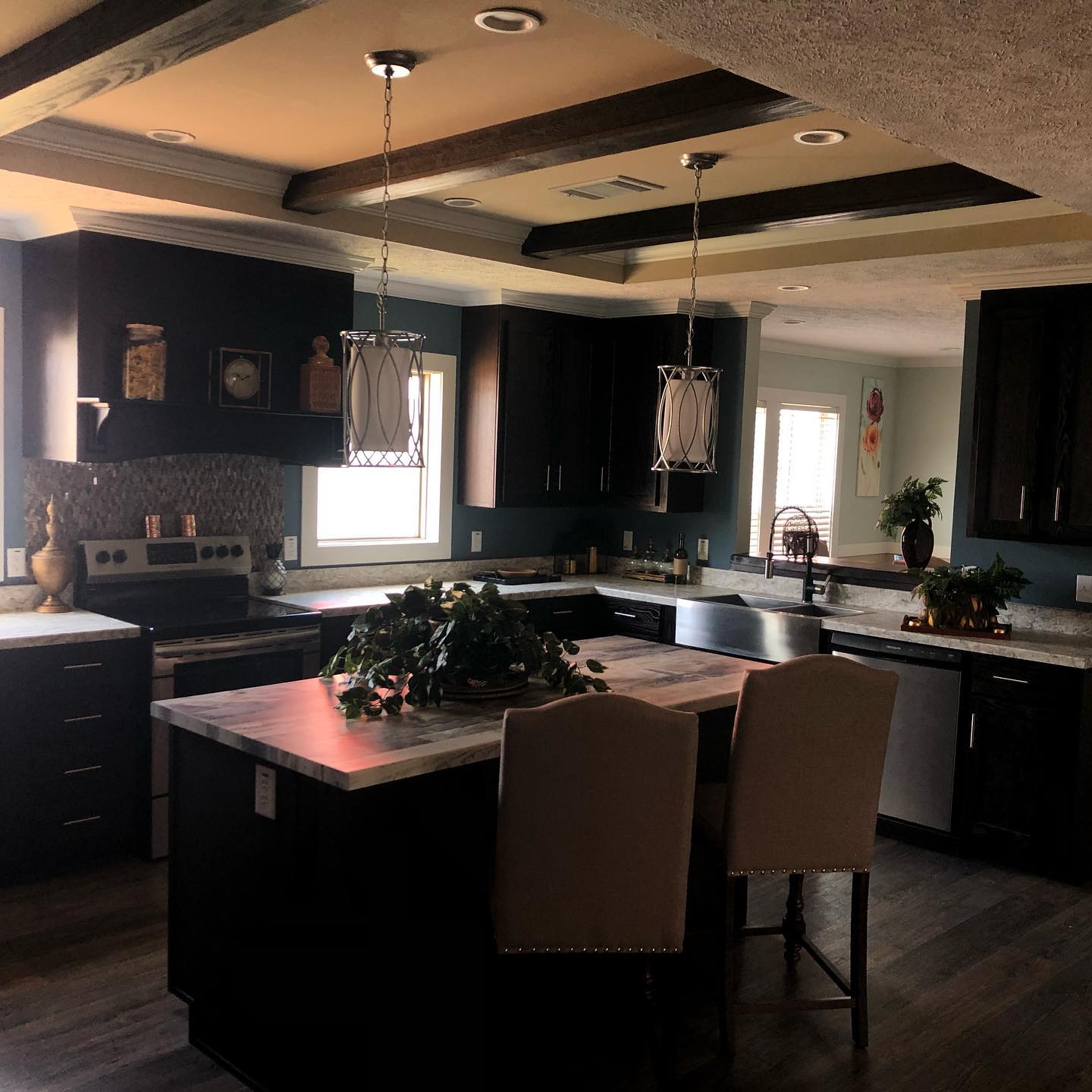 Spacious kitchen with dark wood cabinets, a central island with barstools, pendant lighting, and green plants. Warm, inviting ambiance with natural light.