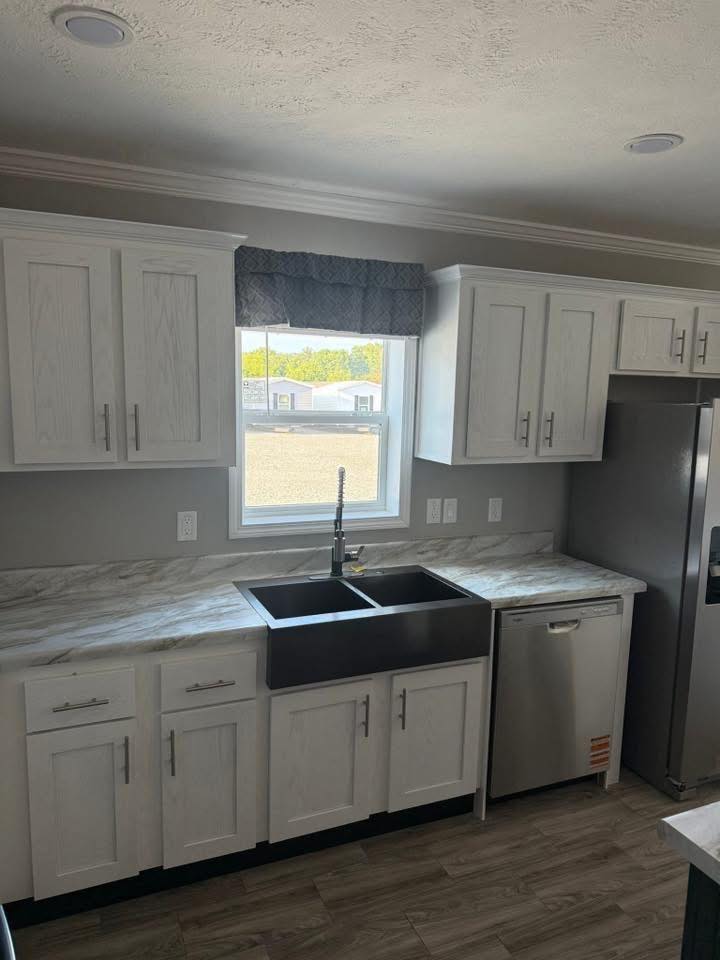 Modern kitchen featuring white cabinets, marble countertops, a double sink, stainless steel dishwasher, and a window with a view. Bright and clean.
