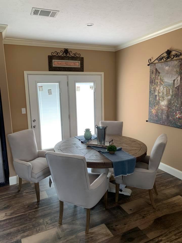 Bright dining area with a round wooden table, four upholstered chairs, and a decorative blue runner. Sunlight streams through glass doors, creating a warm ambiance.