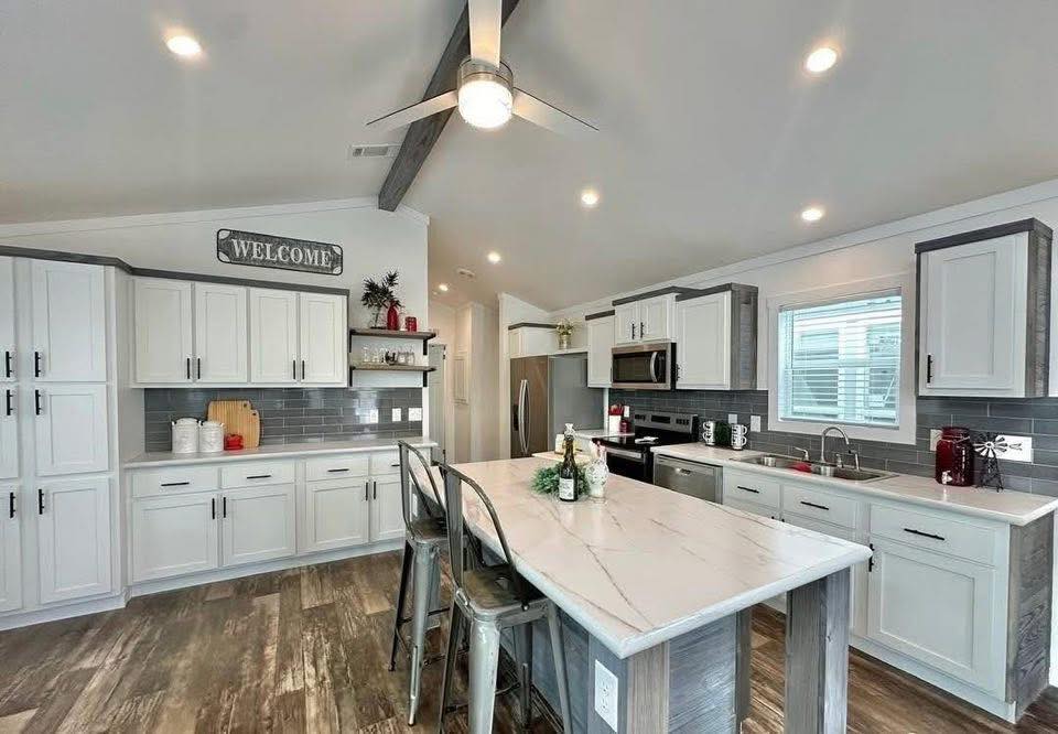 Modern kitchen with white cabinetry, marble island, and stainless steel appliances. Warm wood flooring and gray tile backsplash create a welcoming vibe.