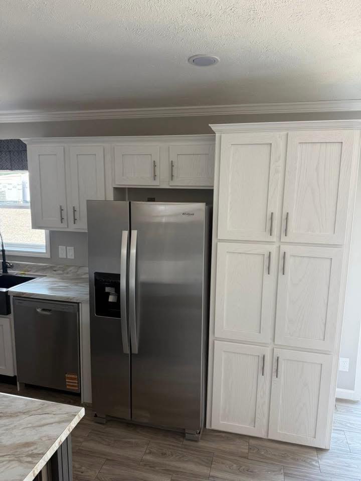 Modern kitchen with a stainless steel refrigerator, white cabinets, and marbled countertops. The space is bright and clean with a subtle contemporary feel.