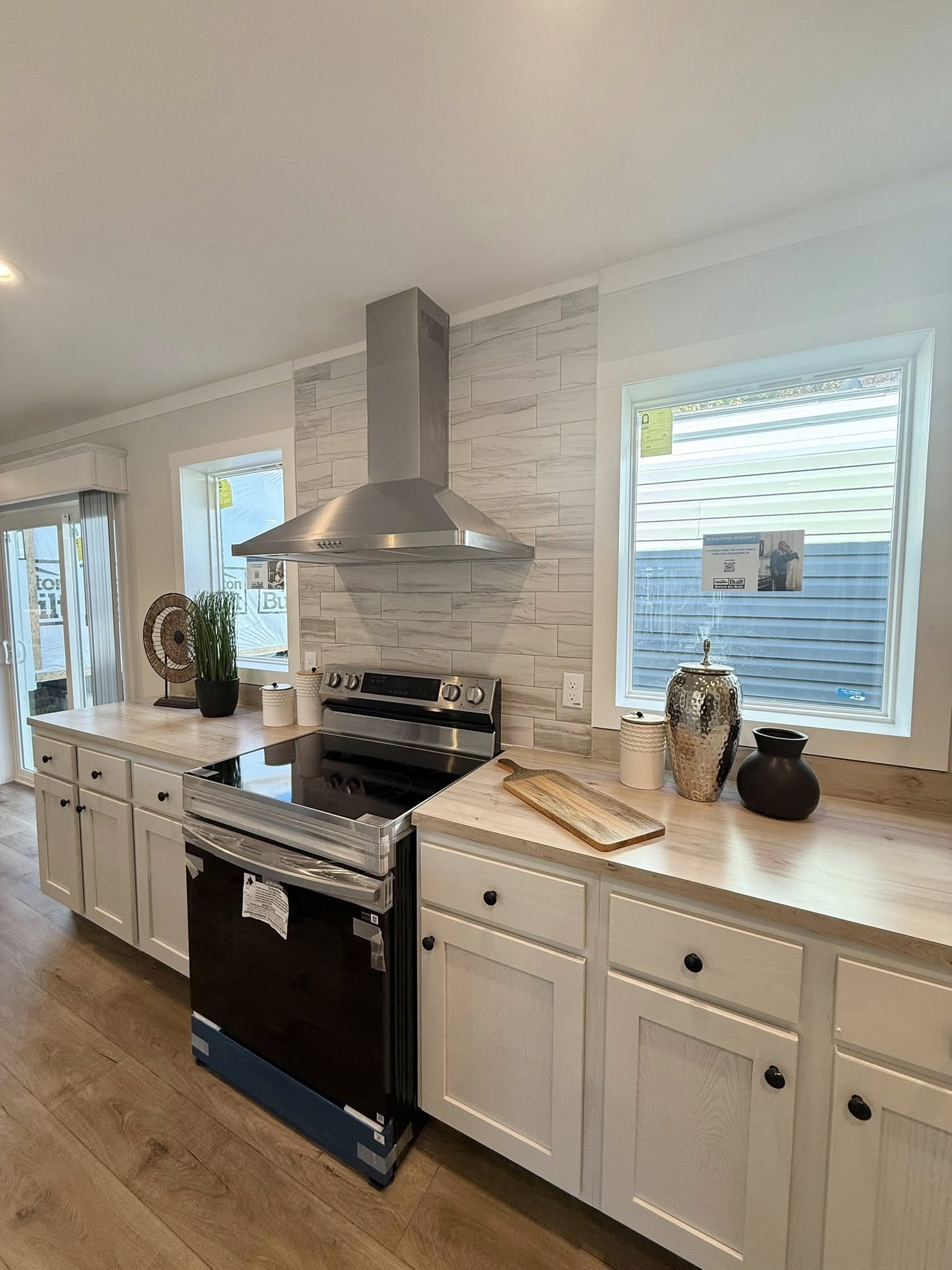 Modern kitchen with stainless steel stove, range hood, and light wood cabinets. Decor includes plants, pottery, and a cutting board, creating a warm, inviting tone.