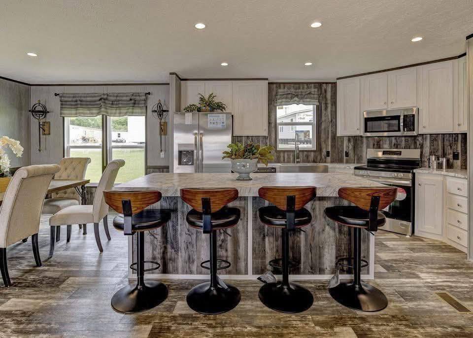 Modern kitchen with a rustic feel, featuring a large island with four wooden stools, stainless steel appliances, and wood-panel flooring. Cozy and inviting atmosphere.