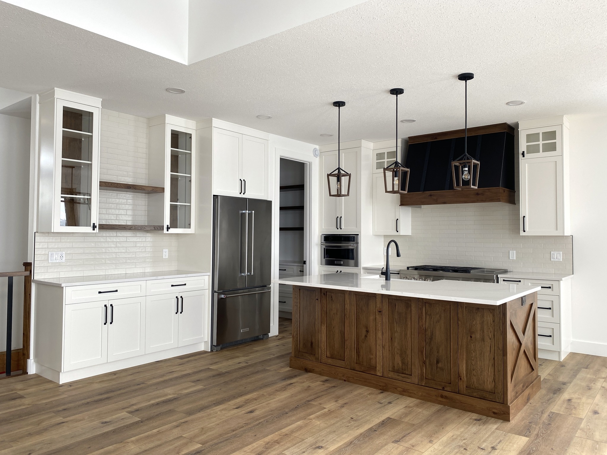 Spacious kitchen with a large wooden island, white cabinets, stainless steel fridge, and black lantern-style pendant lights. Modern and inviting atmosphere.