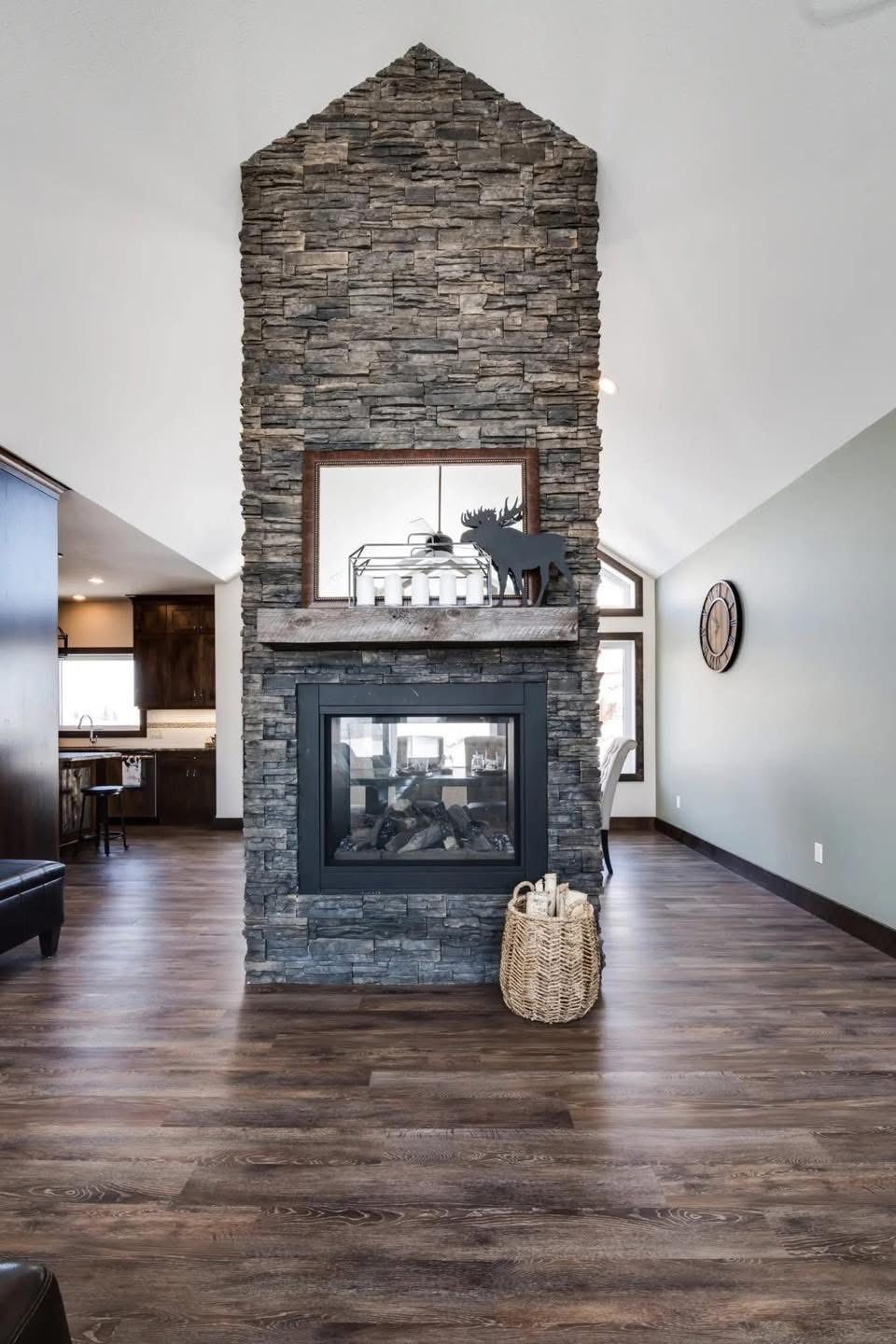 A cozy living room features a tall, stone fireplace with a rustic decor item on the mantel. Hardwood floors and soft lighting create a warm, inviting atmosphere.