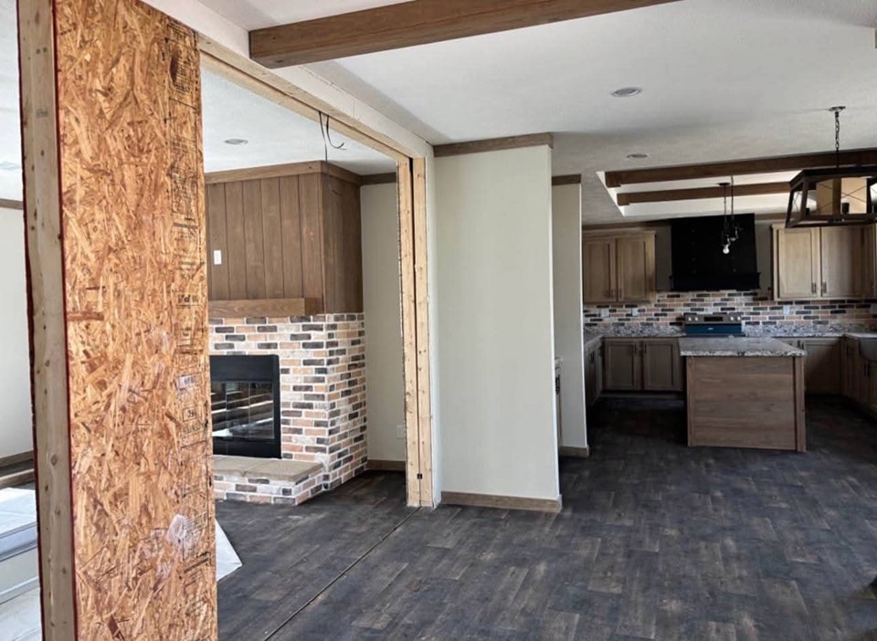 A partially completed interior features an open-floor plan with a wooden floor and brick accents. A fireplace and kitchen with modern cabinets are visible.