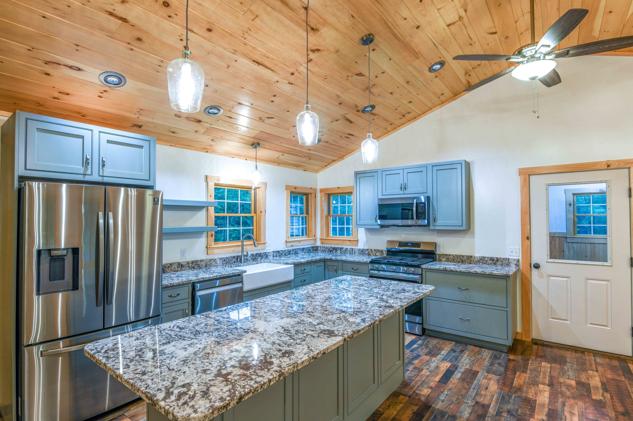 Rustic kitchen with light wood ceiling, modern gray cabinets, and stainless steel appliances. Granite countertops and pendant lighting enhance warmth.