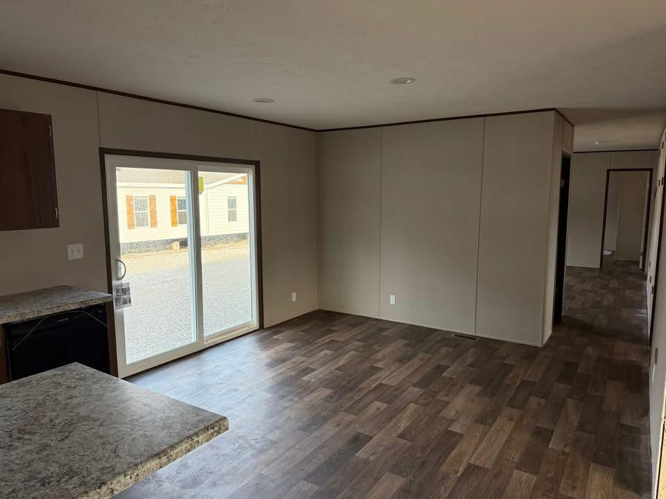 Empty room with brown laminate flooring, beige walls, and a sliding glass door letting in natural light. Modern, neutral tone, spacious feel.