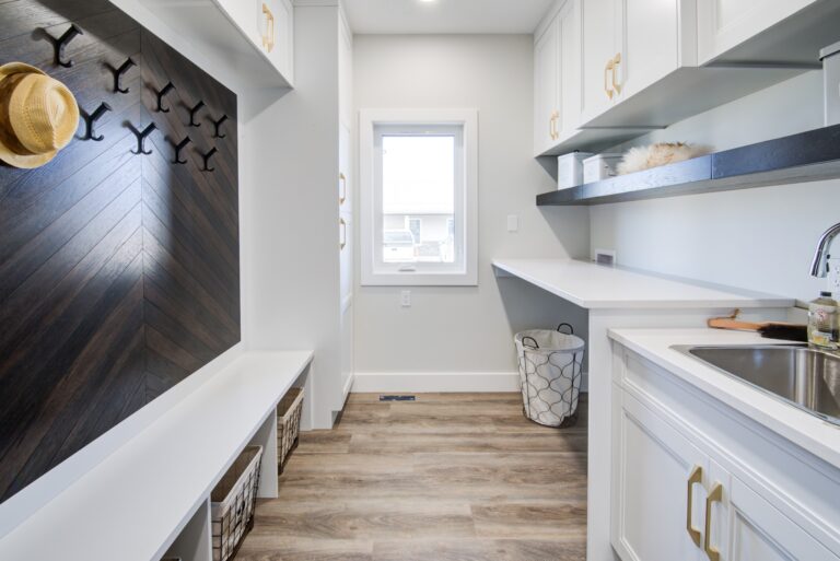 Modern mudroom with a clean, bright aesthetic. White cabinets, a black hook wall with hats, light wood flooring, and a sleek sink convey organization.