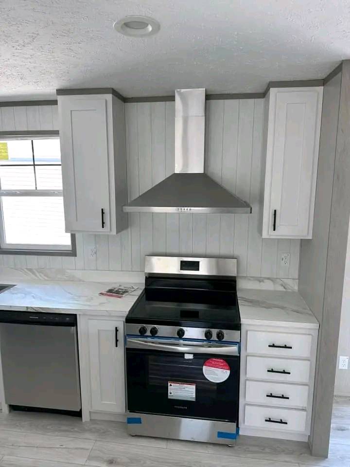 Modern kitchen with stainless steel appliances, including a stove and range hood, surrounded by white cabinets and marble countertops. Bright, clean, and sleek design.