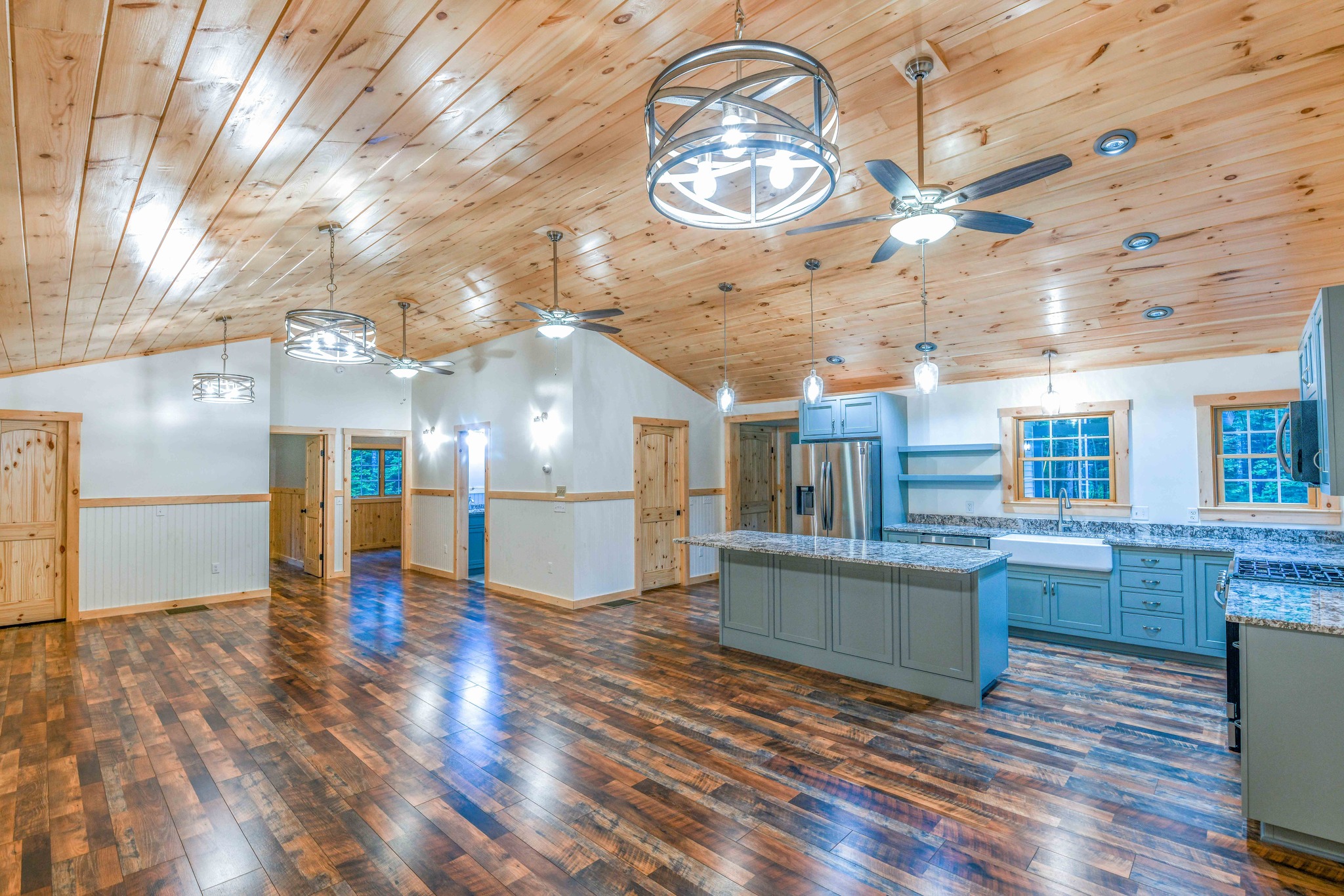 Spacious kitchen with wooden floors and ceilings, modern gray cabinets, stainless steel appliances, and large light fixtures. Cozy and rustic vibe.