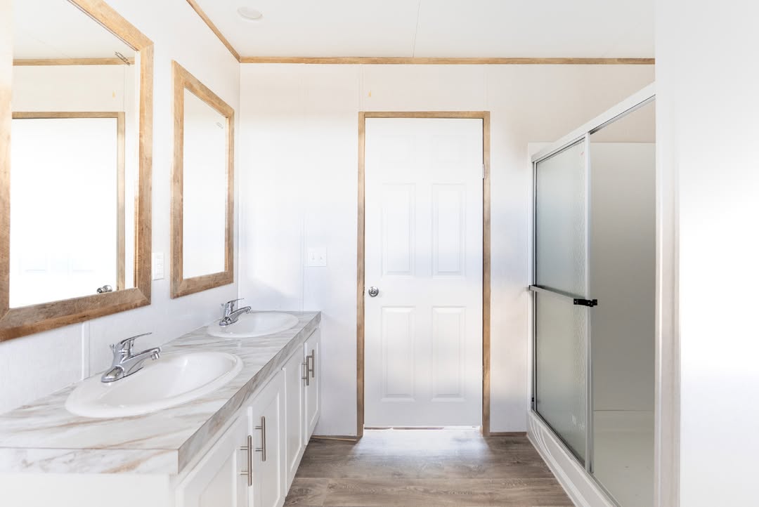 Bright, minimalist bathroom with dual sinks, wooden mirrors, white cabinets, and a glass shower door. Natural light creates a clean, serene ambiance.