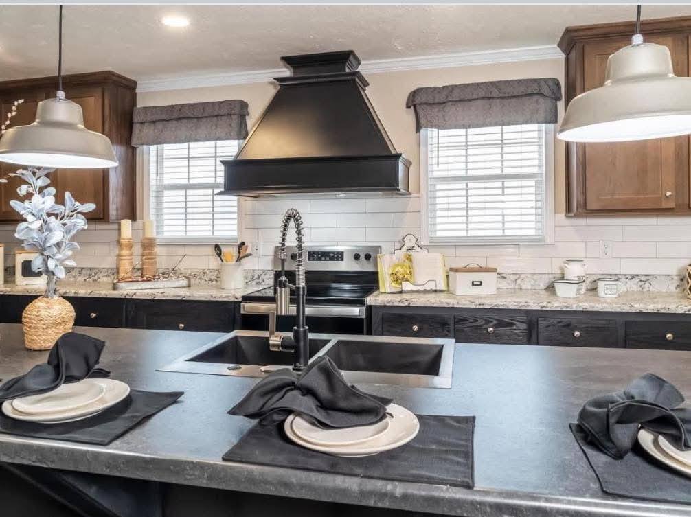 Modern kitchen with a dark island, set with plates and black napkins. Stainless steel appliances, black range hood, and pendant lights create a stylish atmosphere.