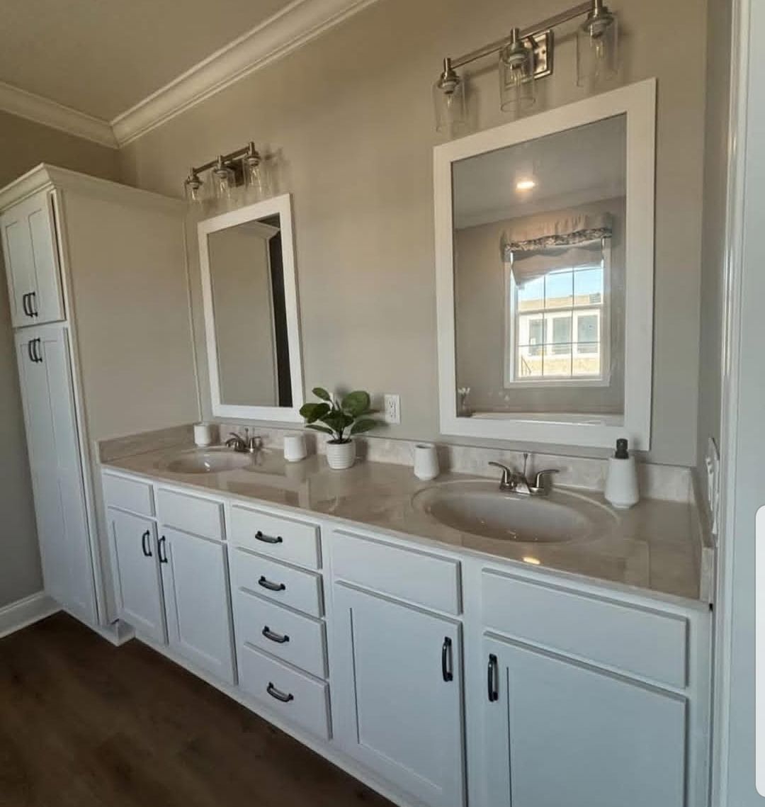 Modern bathroom with a double vanity featuring white cabinets and marble countertops. Two mirrors and plants add elegance under soft lighting.