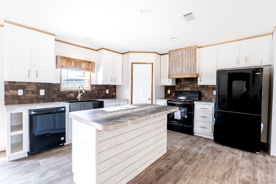 Bright kitchen with white cabinets and dark appliances, including a black fridge and stove. Wood accents, island with rustic countertop, and warm lighting create a cozy atmosphere.