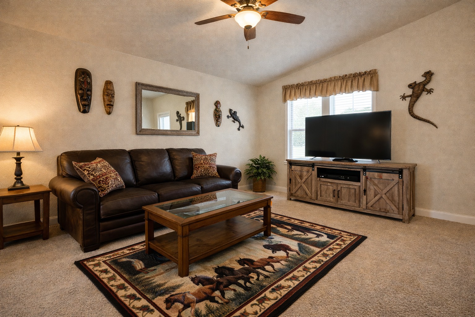 Cozy living room with a leather sofa, glass coffee table on a horse-patterned rug, large TV on a wooden stand, wall art, and warm lighting.