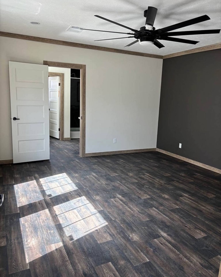A vacant room with dark hardwood floors, gray accent wall, and white walls. Open door reveals another room. A black ceiling fan hangs overhead.