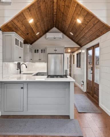 Warm, inviting kitchen with vaulted wooden ceiling, white shiplap walls, sleek gray cabinetry, and stainless steel appliances. Hardwood floor adds to coziness.