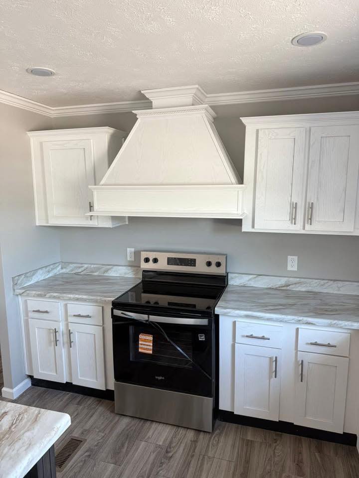 Modern kitchen with white cabinetry, a sleek stainless steel stove, and marble countertops. The room conveys a clean, minimalist aesthetic.