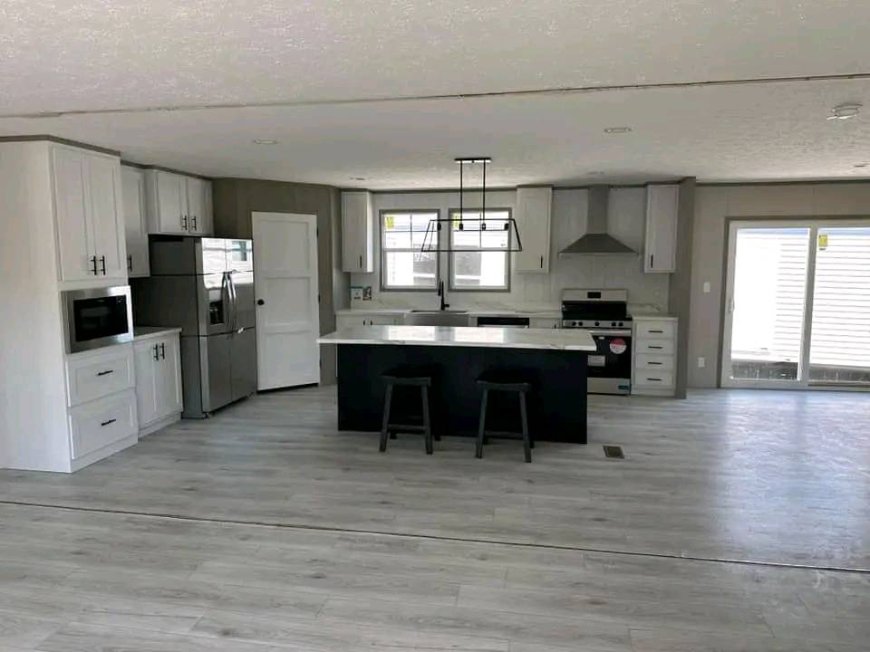 Spacious modern kitchen with white cabinets, stainless steel appliances, large island with stools, and sliding glass doors. Bright and inviting atmosphere.