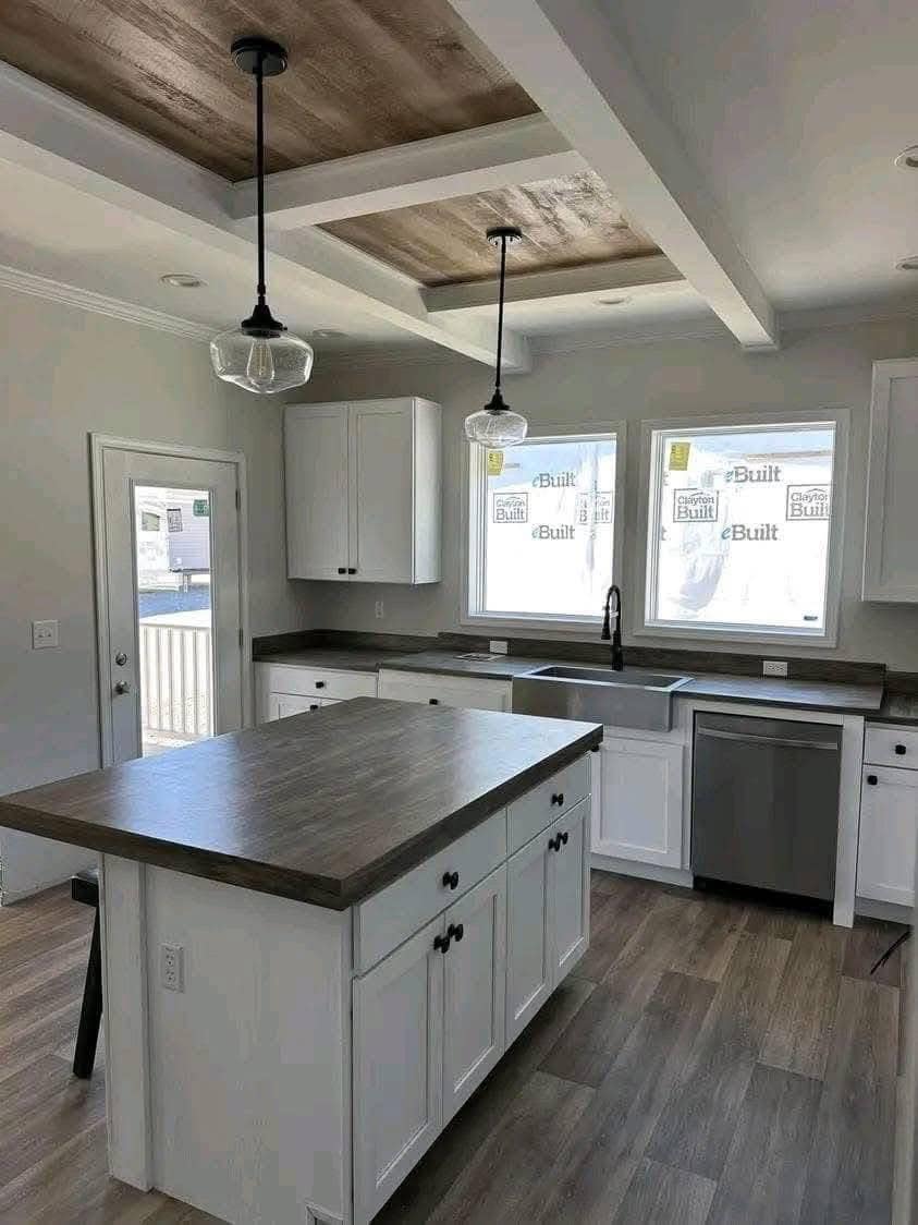 Modern kitchen with white cabinets, dark countertops, and a central island. Two pendant lights hang from a wooden ceiling inset, creating a warm and inviting atmosphere.