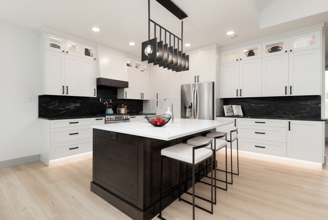 Modern kitchen with white cabinets, black marble backsplash, and a central island with dark wood base and white countertop. Sleek pendant lights hang above, creating a clean, elegant tone.