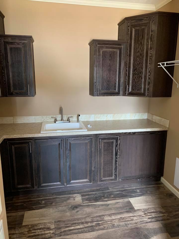 Laundry room with dark wood cabinets above and below a light beige countertop. A white sink with a silver faucet is centered. The floor is dark wood.