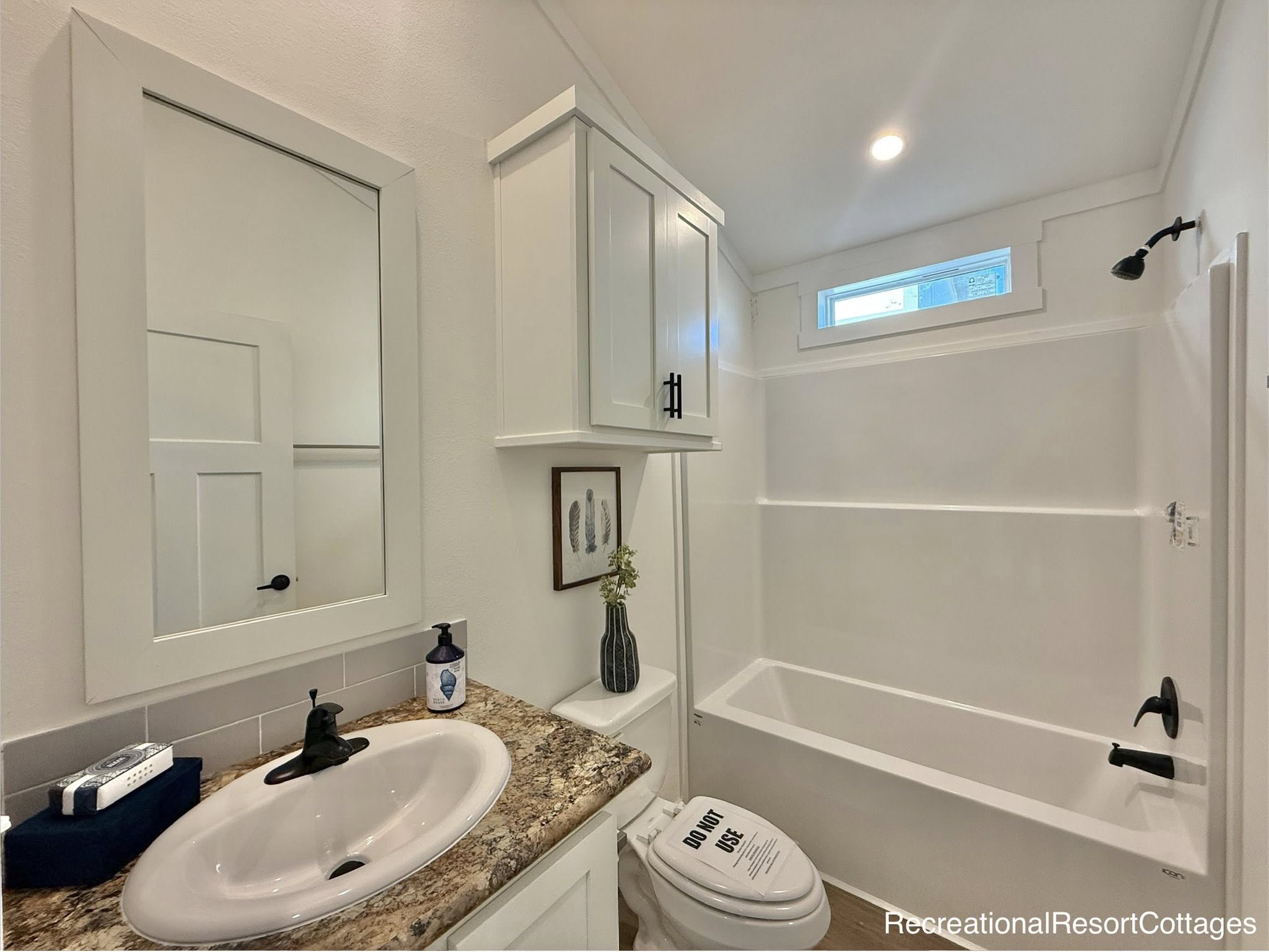 Small modern bathroom with white walls, a granite countertop, sink, and mirror. A shower-tub combo is on the right; a vase and artwork add decor.