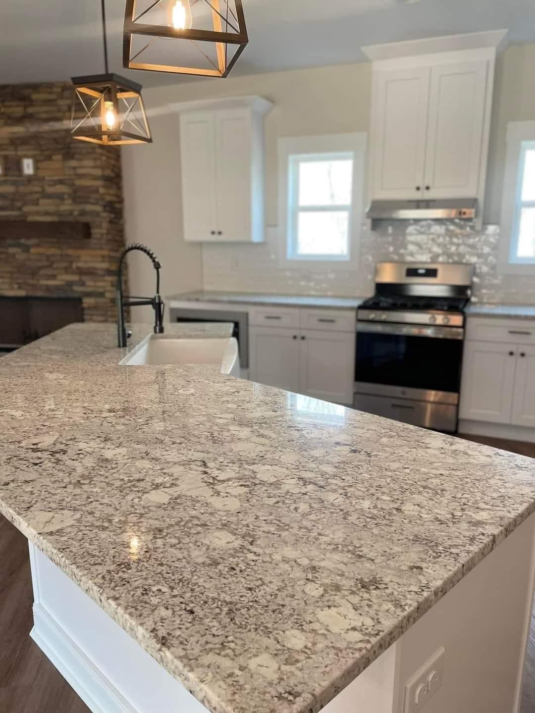 Modern kitchen with granite countertops, stainless steel appliances, and white cabinets. Pendant lights hang above, creating a bright, elegant ambiance.