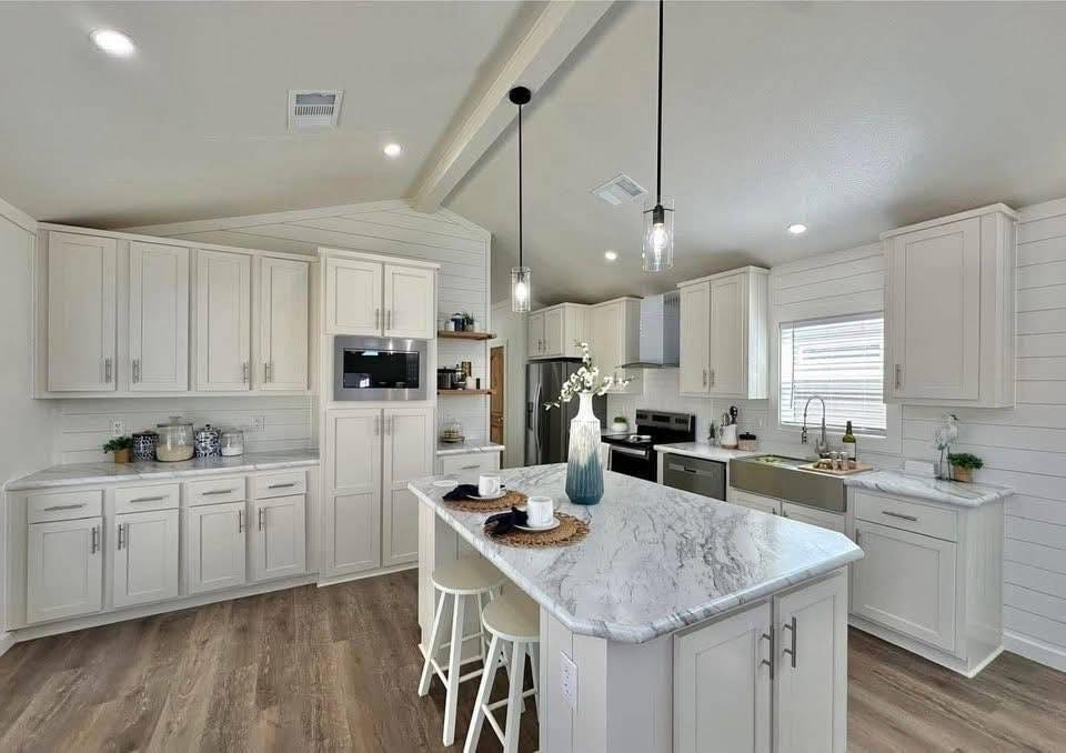 Modern kitchen with white cabinets, marble countertops, and wood flooring. Center island with stools, pendant lighting, and a bright, airy ambiance.