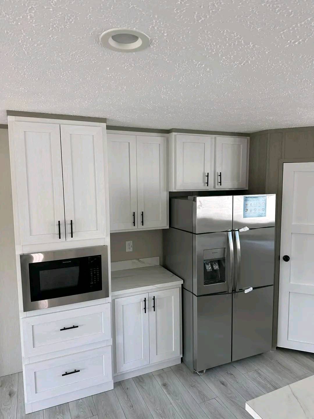 Modern kitchen with white cabinets, a stainless steel fridge, and a built-in microwave. Light wood flooring adds a bright, clean feel.