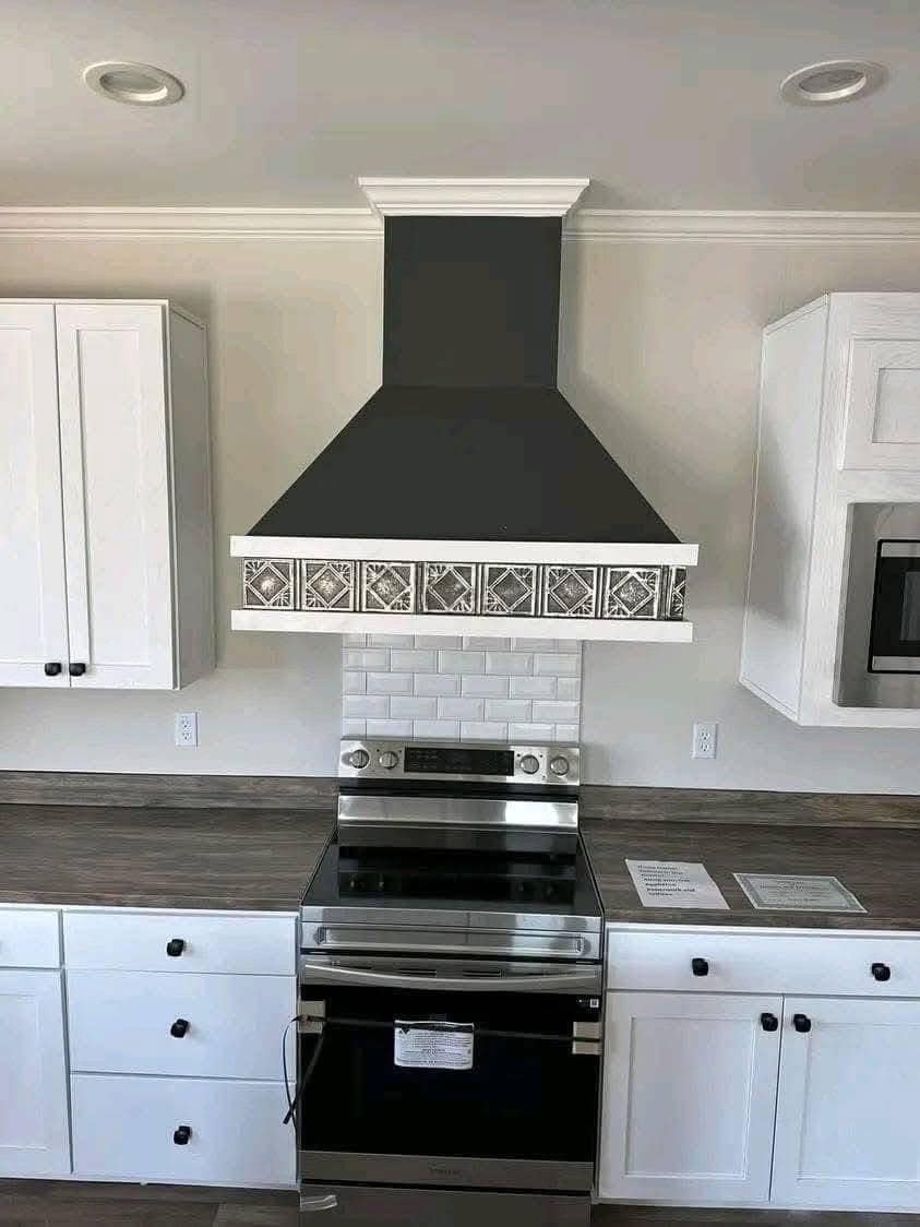Modern kitchen with a black range hood featuring patterned tiles, above a stainless steel stove. White cabinets and subway tile backsplash create a sleek look.