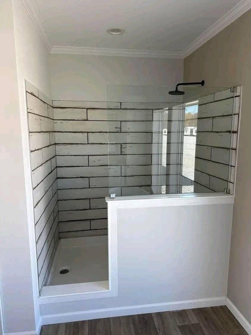 Small modern shower with glass partition, wood-like tile walls, and a rainfall showerhead. The space is compact, minimalistic, with a cozy feel.